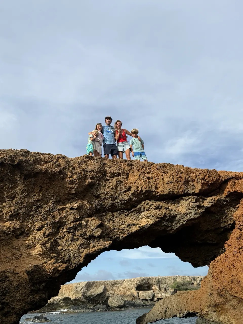 Our family of five standing on top of a natural rock arch on a rugged, rocky coast